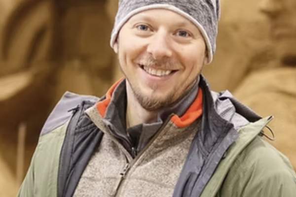 Portrait of Ilya Filimontsev smiling and wearing a grey beanie and green outdoor jacket.
