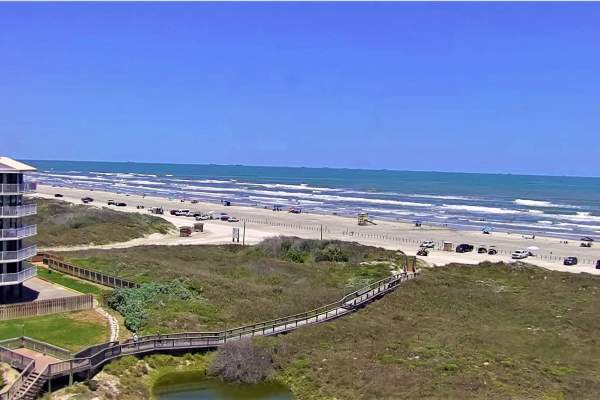 Photo of the view from a webcam showing the sand dunes, a boardwalk, and the beach.