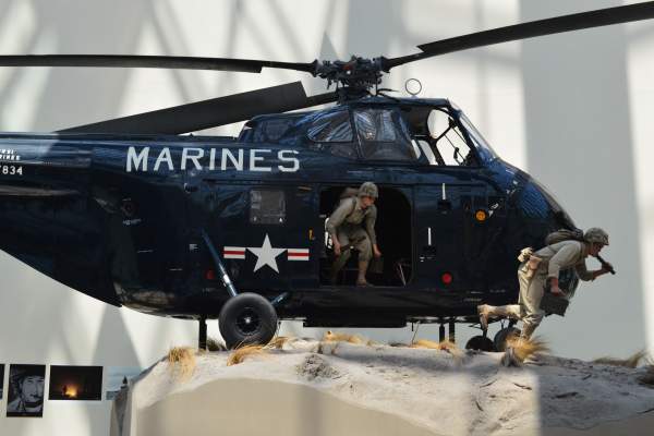 a navy helicopter with the word "marines" on the front with 2 statues of men coming out of the helicopter