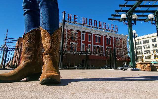 Woman in cowgirl boots stands in the foreground with the Wrangler behind her in Downtown Cheyenne, Wyoming