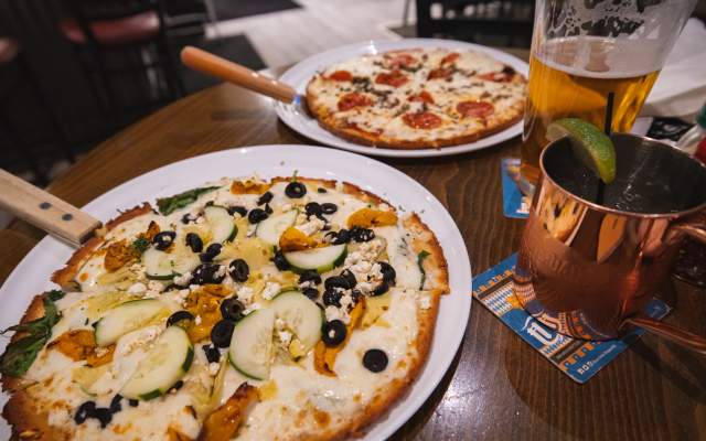 Two pizzas with sit on a table in a restaurant with drinks