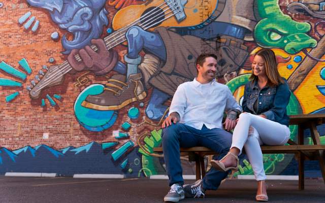 A couple sits on a bench talking with a giant mural behind them