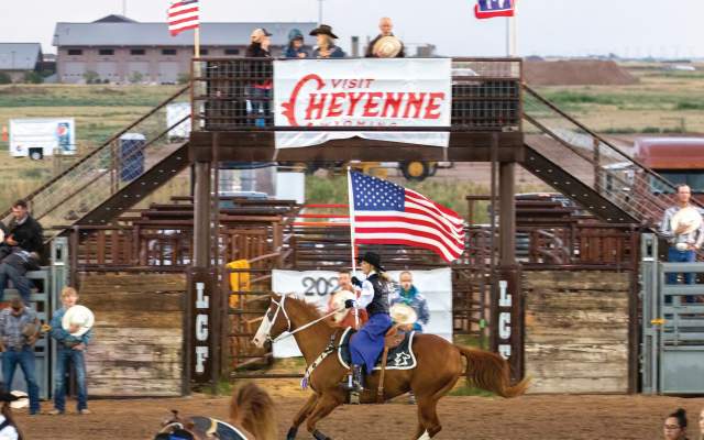 A horse and rider cary the American Flag into a rodeo arena