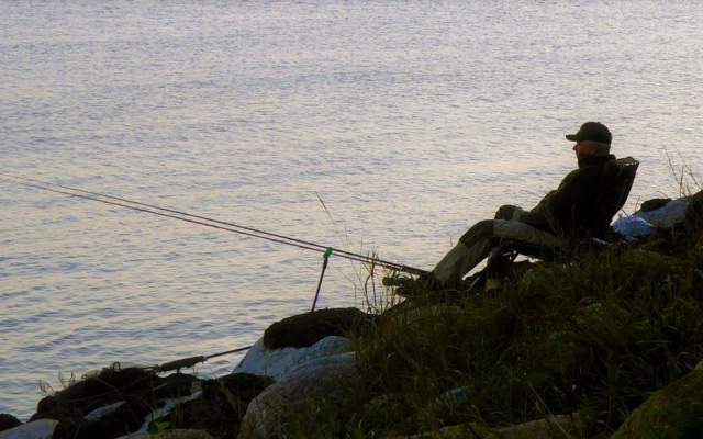 Man sitting at lake shore, watching his fishing poles.