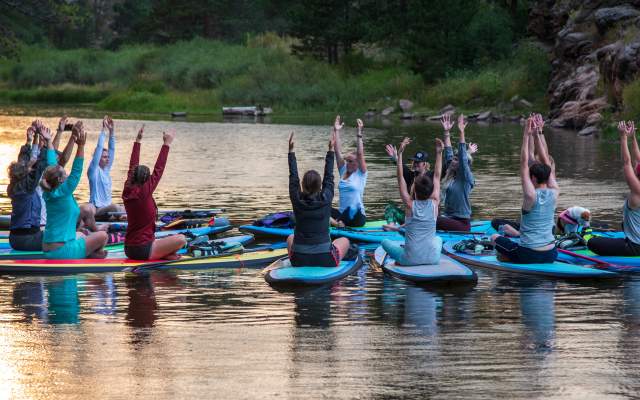 More than a dozen females sitting on paddleboats, floating on the water, and doing yoga.