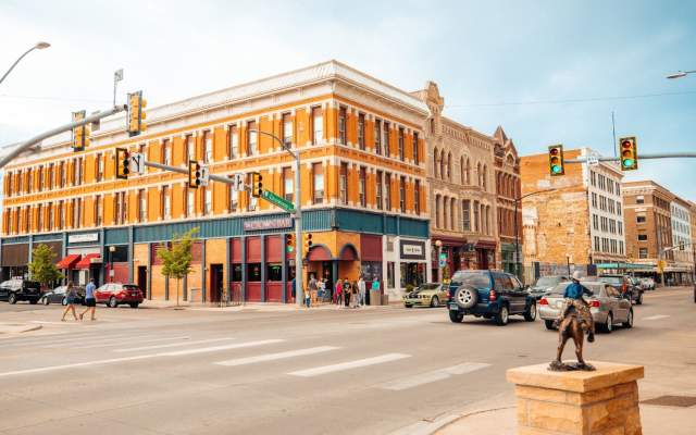 A photo taken from the southwest corner of Lincolnway and Carey Avenue facing the Crown Bar. There is a bronze statue, pedestrians, and traffic.