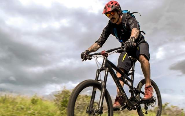 A bicyclist on a mountain bike riding in an open field with a story sky behind him.