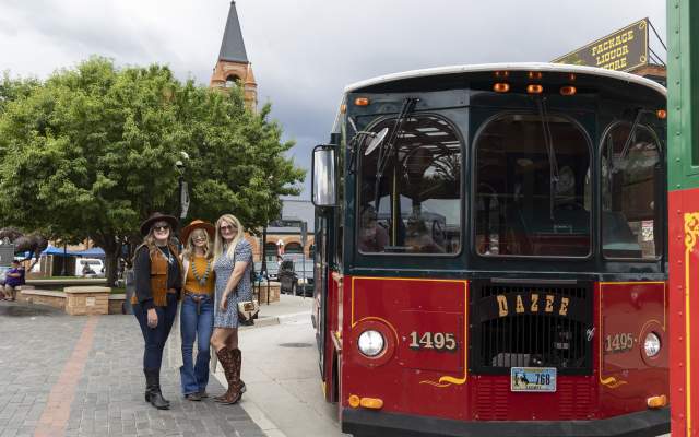 A group of three young women standing by the trolley in front of the Depot
