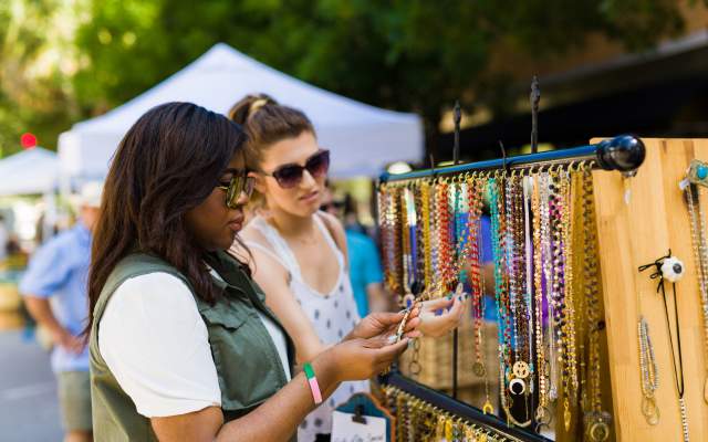 two women shop jewelry at an outdoor market stall