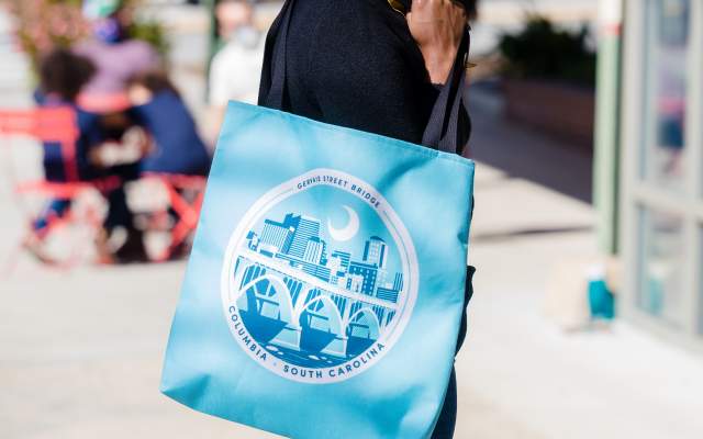 Woman holding blue tote bag while standing on sidewalk