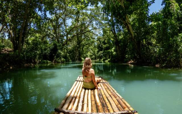 A woman in a green swinsuit sits on a bamboo raft on the Martha Brae River in Montego Bay Jamaica