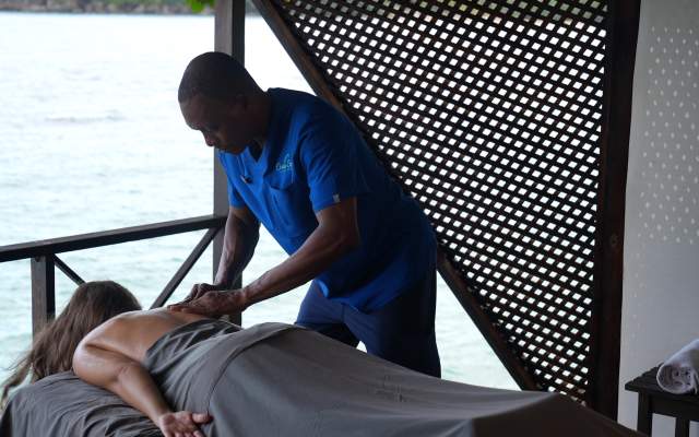 A woman lies on a massage table as a man massages her back overlooking the sea