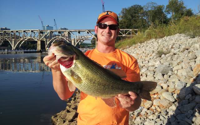 Man holding small mouth bass on shore of Tennessee River