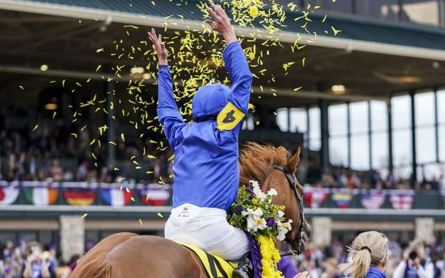 A jockey in blue and yellow silks celebrating a win atop a thoroughbred horse amidst yellow confetti at Keeneland.