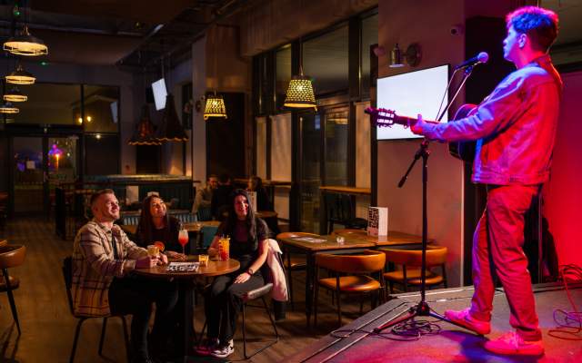 Group of friends sitting around a table watching a musician on stage