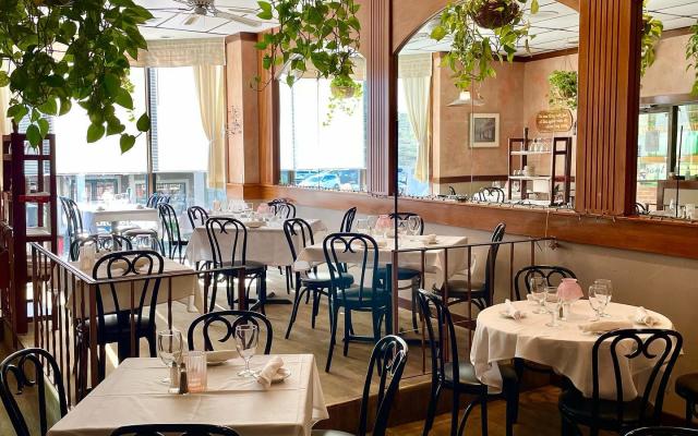 A dining area with white tablecloths, black chairs, and hanging plants.