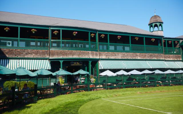 A large building with green trim and a balcony overlooking a grassy area with a tennis court.