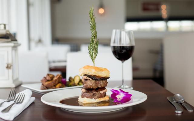 A plate of food with a sandwich, garnish, and a glass of wine on a table.