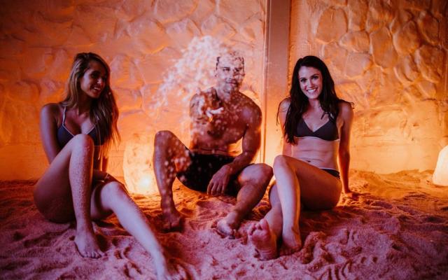 Three people sitting in a salt room with dim orange lighting.