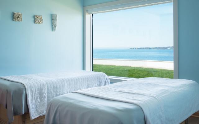 a serene spa room with two massage beds and a large window overlooking the ocean