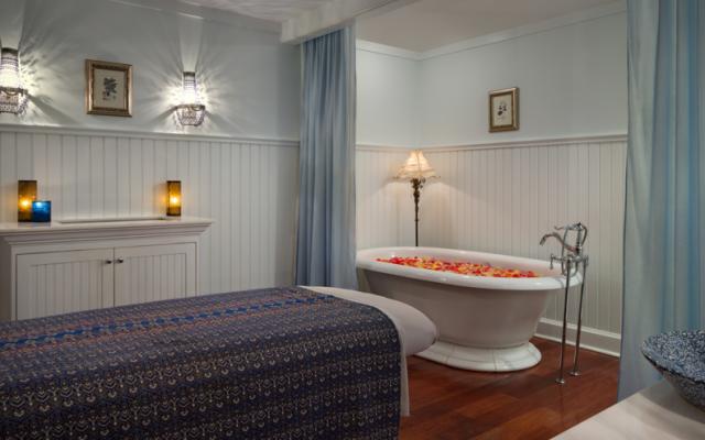 A luxurious bedroom with a large bed and a bathtub filled with flowers.