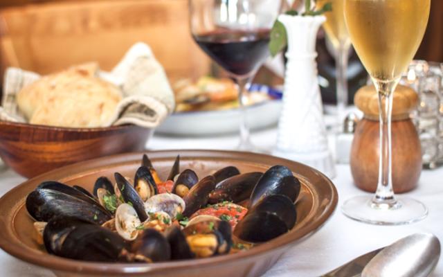A plate of mussels with a glass of wine and bread on the table.