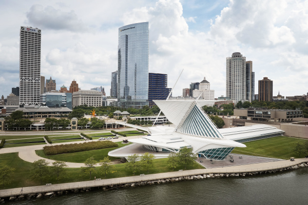 Milwaukee skyline featuring the Milwaukee Art Museum’s iconic white Quadracci Pavilion with its wing-like Burke Brise Soleil along Lake Michigan, surrounded by downtown high-rise buildings including the US Bank Center and Northwestern Mutual Tower under a partly cloudy sky.