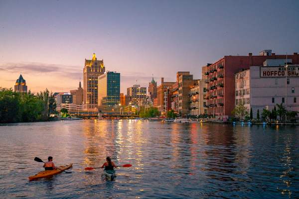 two kayakers on the Milwaukee River overlooking Milwaukee's Historic Third Ward and the skyline