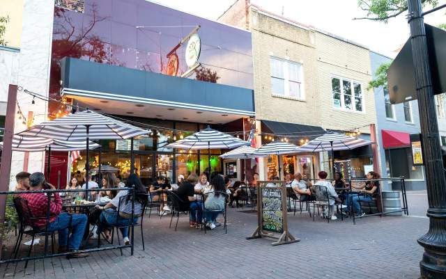 People enjoying outdoor dining under striped umbrellas and string lights in downtown Fayetteville.