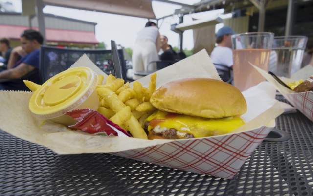 Close-up of a basket with a cheeseburger, French fries, and condiments on an outdoor restaurant table in Hope Mills, NC