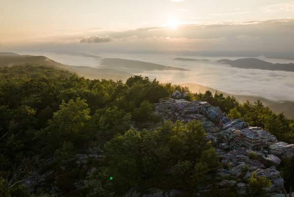 Sunrise over the Appalachian Mountains from Dan’s Rock Scenic Overlook in Dans Mountain State Park, with a rocky viewing platform surrounded by forest and a valley filled with morning fog.