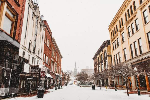 Fresh snow covers the quiet street, with large architecturally ornate buildings bordering the downtown.