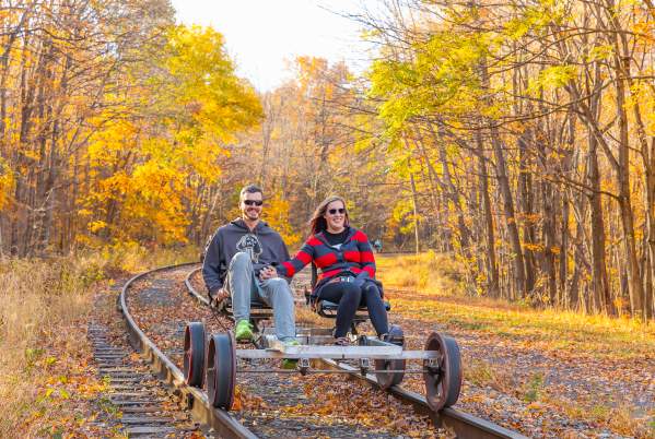 A couple peddles on a rail bike riding along the rail line in the fall.
