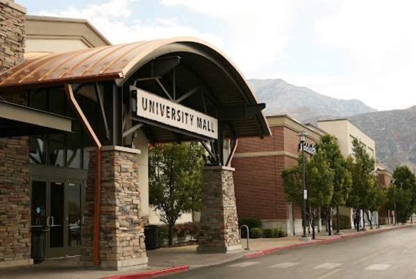 University Place main South door to mall. Sign above door reads "University Mall." Verge trees along sidewalks. Mountains are visible far away in the background.
