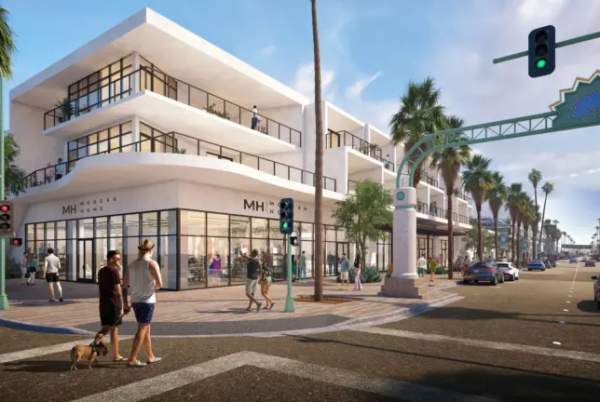 A sunny streetscape with modern two-story white buildings on the left, palm trees lining the road, pedestrians, some with a dog, crossing the street, cars on the road, and a traffic light showing green.