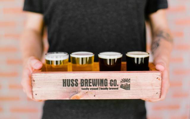 A server holds a flight of beers in a branded Huss Brewing box