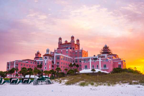 The Don CeSar resort hotel in St. Pete Beach glows hot pink as the sun rises from behind in the east.