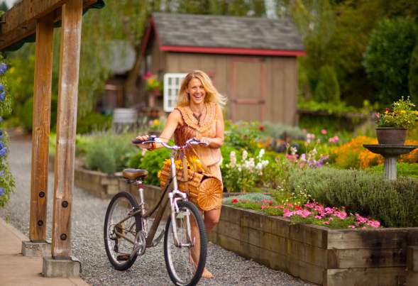 woman in orange dress walks bikes past garden