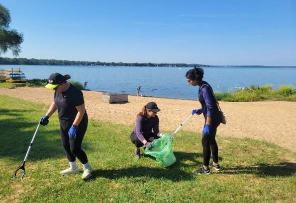 Three women clean up garbage on a beach in Madison, WI
