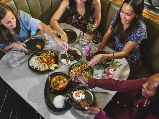 Group of women enjoying various appetizers and meals at Sense of Thai in a booth.