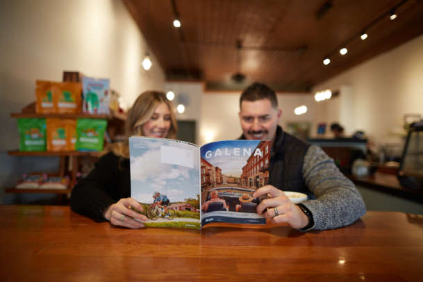 Two people sitting in a coffee shop, holding a Galena Country Visitor's Guide.