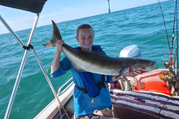 A woman in a boat holding a freshly caught cobia fish, in the waters off Port Hedland