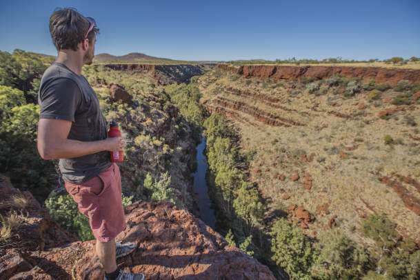 A man stands looking over water flowing through Dales Gorge, in Karijini National Park