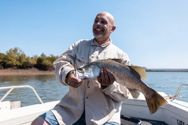 A man holds a barramundi, caught while fishing on the Ord River near Kununurra