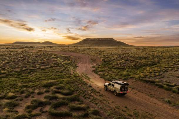 A car driving on an outback track towards a mountain at sunrise