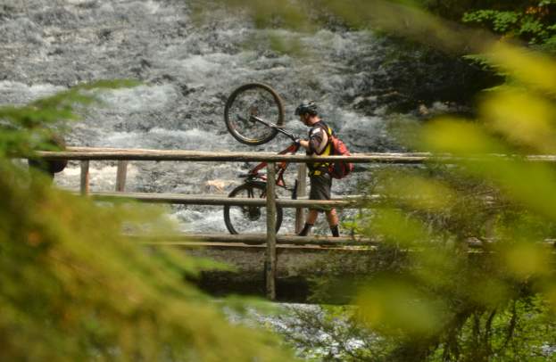 Mountain biker walking bike across bridge.