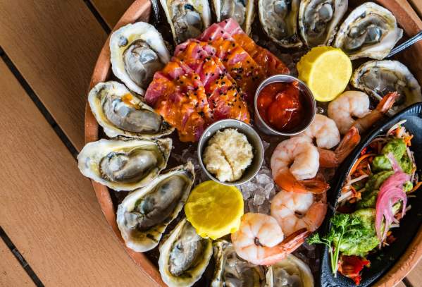 A seafood platter on ice with oysters, shrimp, and tuna.