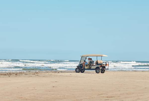 A golf cart sits on the beach in the distance with waves crashing behind.