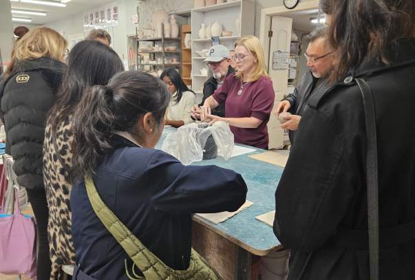 A group of people are gathered around a table working on making pinch pots with clay.
