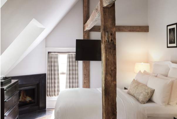 A guest room at the Bedford Post Inn. The room has wooden beams going over the bed and a fireplace can be seen in the background.